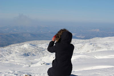 Rear view of woman sitting on snowcapped mountain against sky