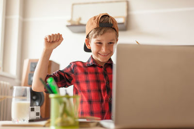 Cheerful boy celebrating his success while using computer in the living room.