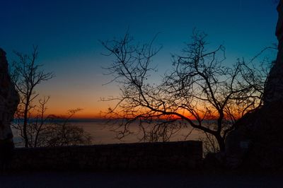 Silhouette bare tree by lake against sky during sunset