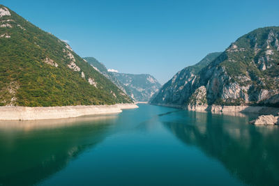 Scenic view of lake and mountains against clear blue sky