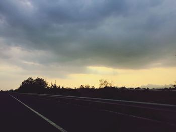 Road by silhouette trees against sky during sunset