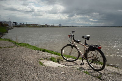 Bicycle parked by river in city against sky