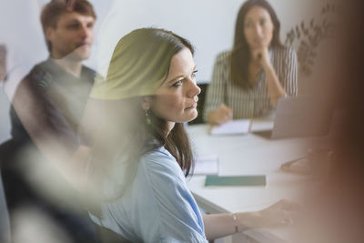 Businesswoman with colleagues listening while sitting at conference table during meeting in office