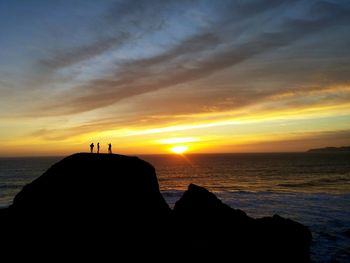 Silhouette rock formation by sea against sky during sunset