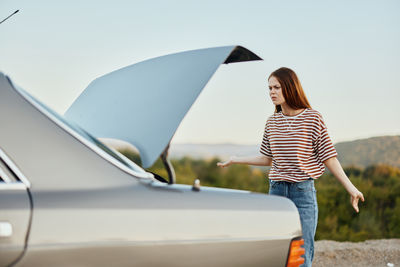 Rear view of woman with umbrella standing against car