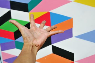 Cropped hand of person gesturing towards colorful wall