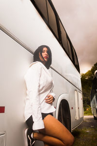 Young woman sitting on car against sky