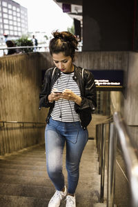 Woman using mobile phone while walking up on steps at subway station