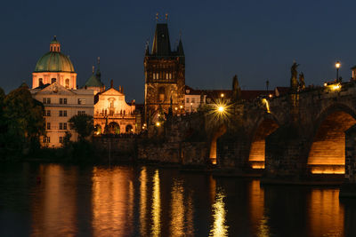 Illuminated buildings by river against sky at night