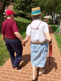 Rear view of senior couple holding hands while walking on footpath in park