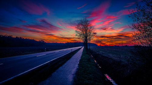 Empty road amidst field against sky during sunset