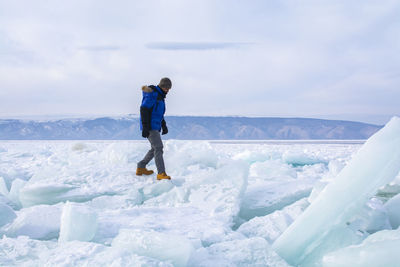Full length of man walking on glacier on frozen lake against sky