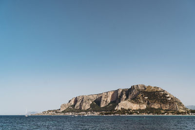 Rock formations by sea against clear blue sky