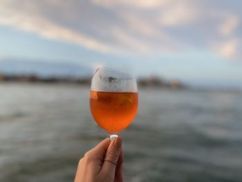 Close-up of hand holding drink against sky