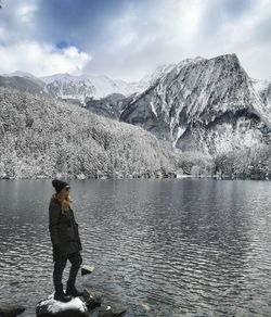 Woman standing at lakeshore against mountains during winter