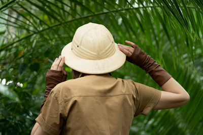 Naturalist in khaki clothes, hat, leaver gloves stands in rainforest with palms. jungle tourist