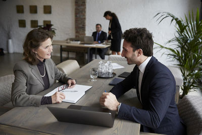 Confident senior female lawyer smiling while discussing over laptop with young businessman during meeting at office