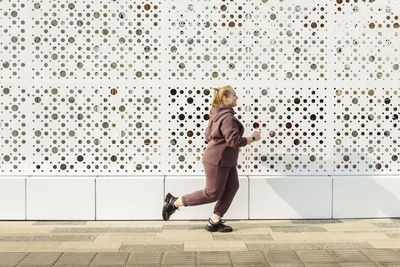 Overweight young woman jogging by wall