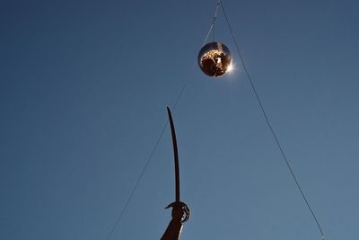 Low angle view of disco ball hanging against clear blue sky