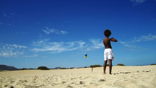 Rear view of boy standing on beach against blue sky