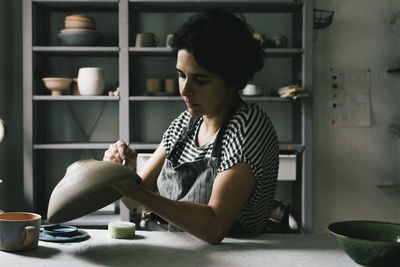 Female owner painting bowl at table in ceramics store