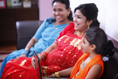 Mother and daughter using laptop while sitting on sofa at home