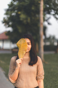 Young woman covering face with leaf while standing outdoors