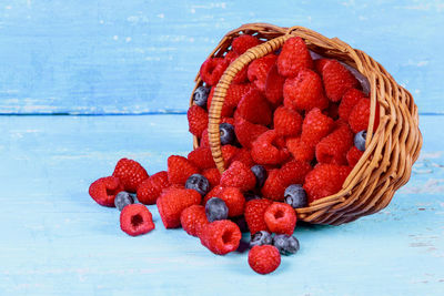 Raspberries and blueberries with basket on wooden table