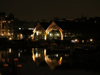 Illuminated buildings by river against sky at night