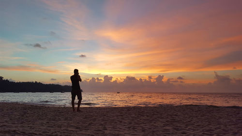 Silhouette woman standing on beach against sky during sunset