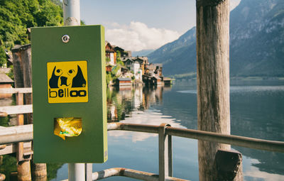 Close-up of sign on wooden post by lake against sky