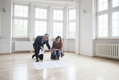 Real estate agent showing construction plan to client in empty apartment