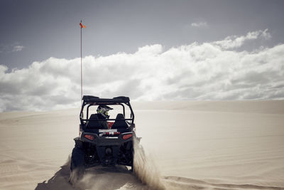 Man driving golf cart on sand at desert against cloudy sky