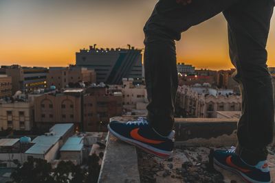 Low section of man and buildings against sky during sunset