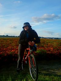 Woman with bicycle on flower field against sky