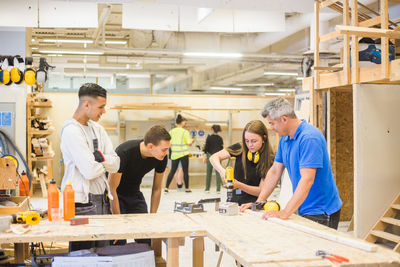 Male instructor and trainees watching while woman using power drill at workbench during training