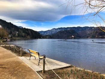 Empty bench by lake against sky