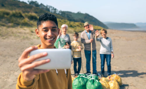Smiling young man photographing with family while cleaning beach