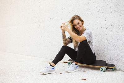 Full length of smiling young woman sitting against wall