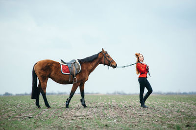 Woman riding horse on field against sky