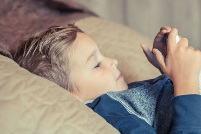 Side view of boy using mobile phone while lying on bed at home