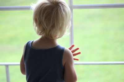 Rear view of boy looking through window at home