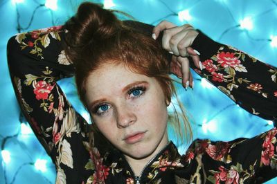 Close-up portrait of young woman against string lights