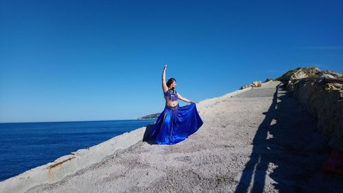 Young woman with umbrella on sea against clear blue sky