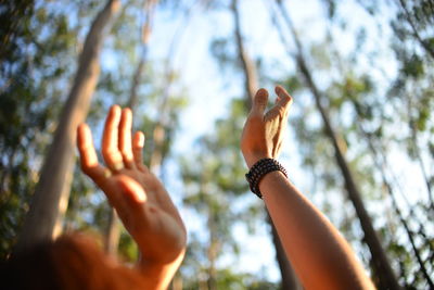 Low angle view of woman with arms raised against trees in forest