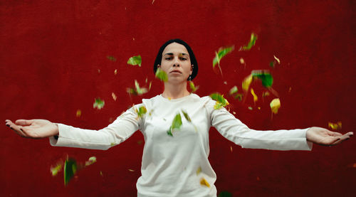 Portrait of woman with arms raised standing against red wall