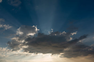 Low angle view of sunlight streaming through clouds