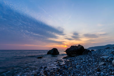 Rocks on beach against sky during sunset