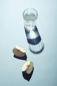 Glass of water and pieces of apple on blue background.