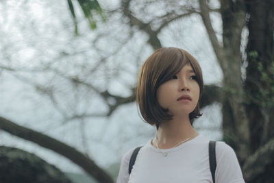 Young woman looking away against tree